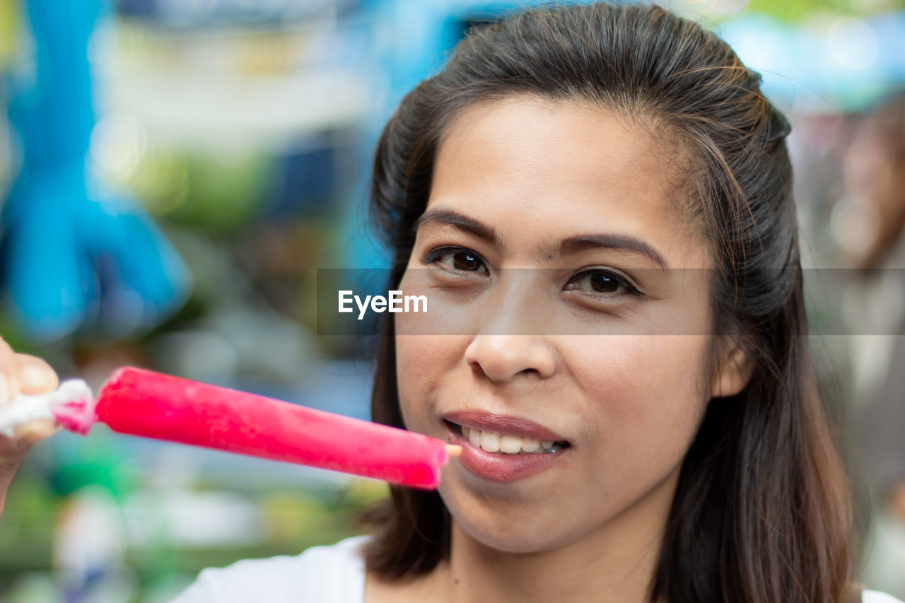 Close-up portrait of woman having pink popsicle outdoors