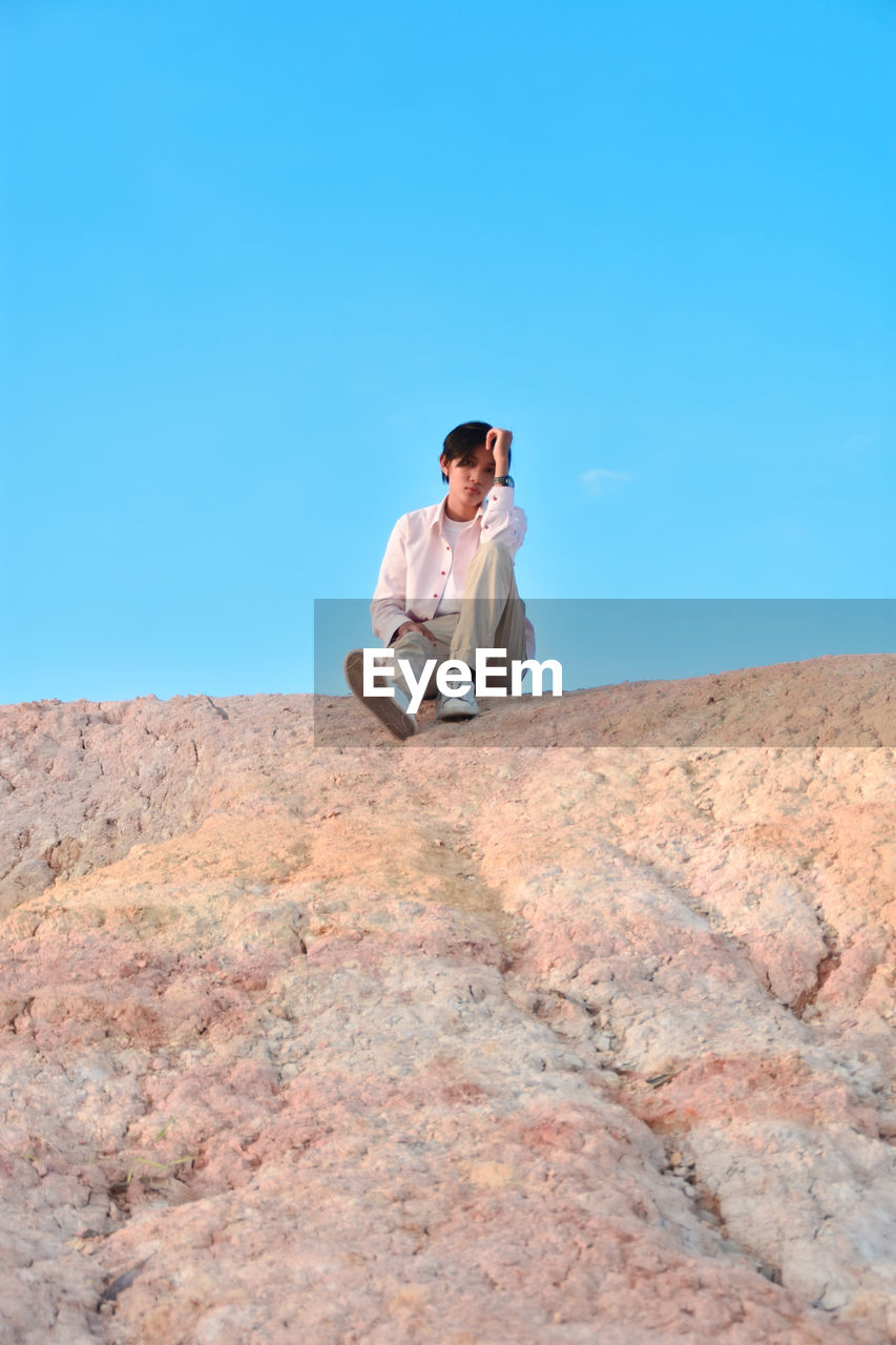 A person sitting on a rock with a bright blue sky