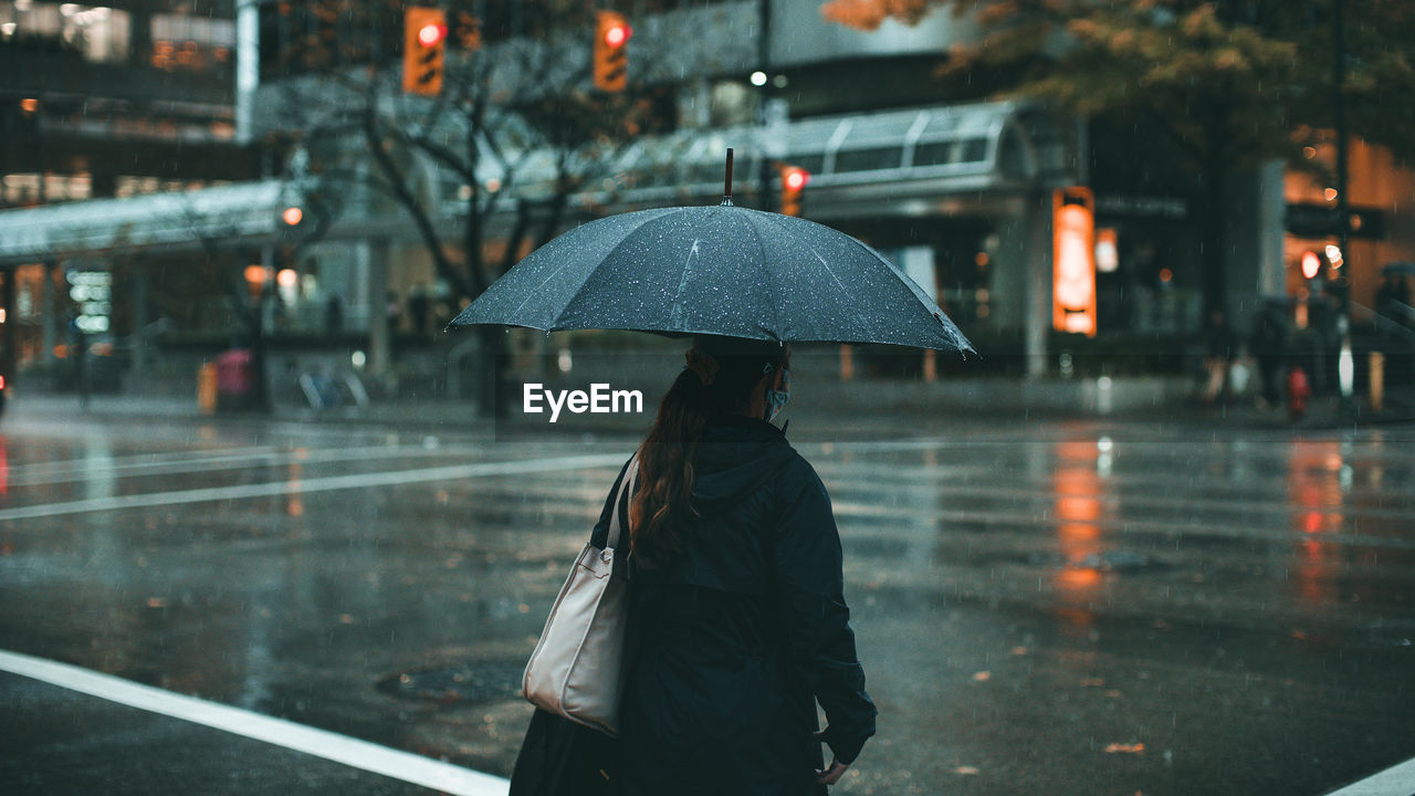 WOMAN WALKING ON WET ROAD DURING RAINY SEASON IN CITY