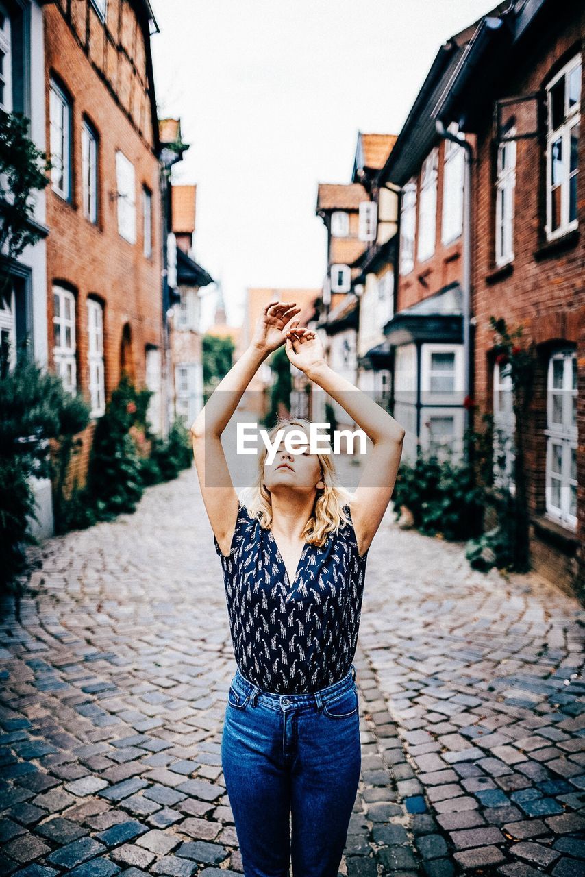 Young woman with eyes closed and arms raised standing on footpath amidst buildings