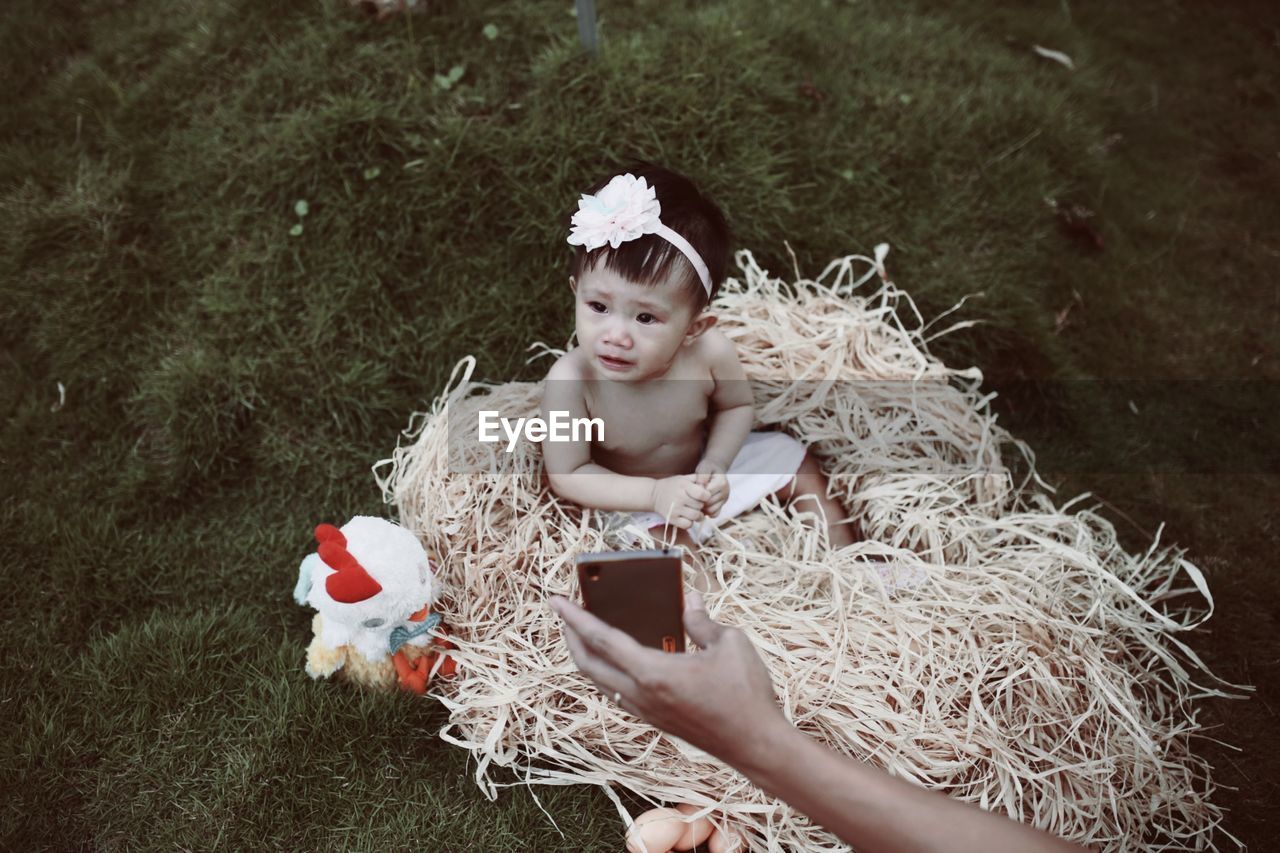 High angle view of topless baby girl sitting on straw at field