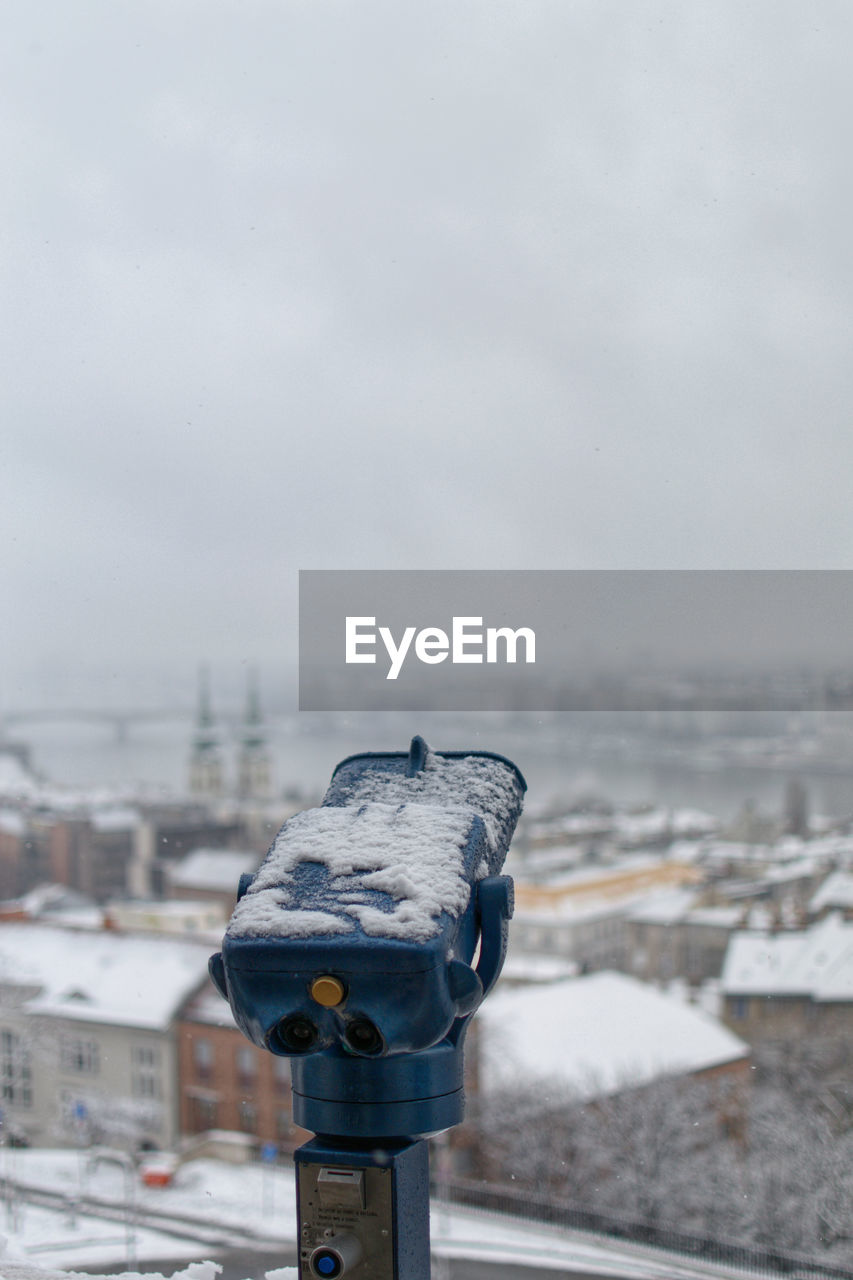 Close-up of coin-operated binoculars against cityscape during winter