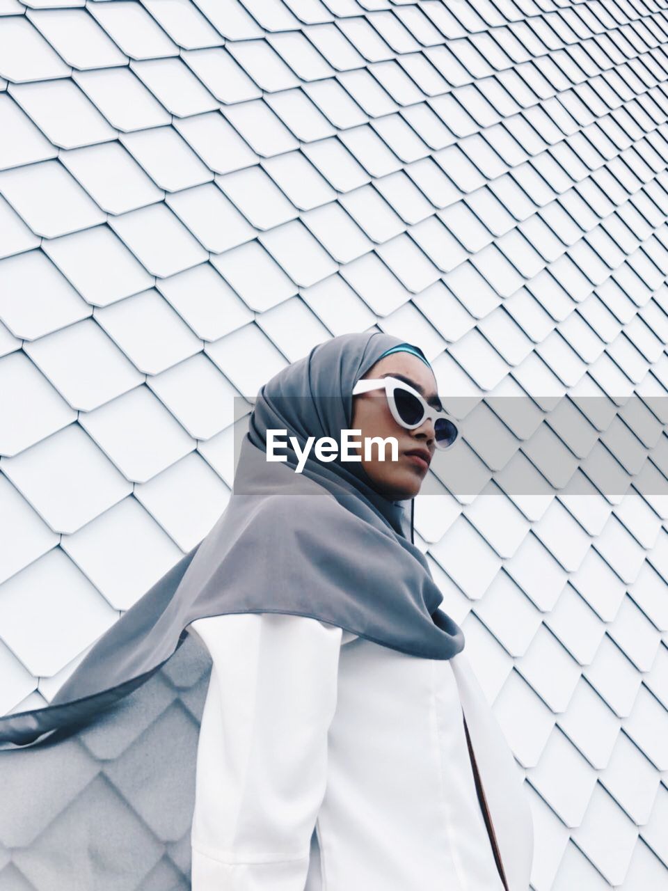 Woman wearing sunglasses and hijab while standing against wall