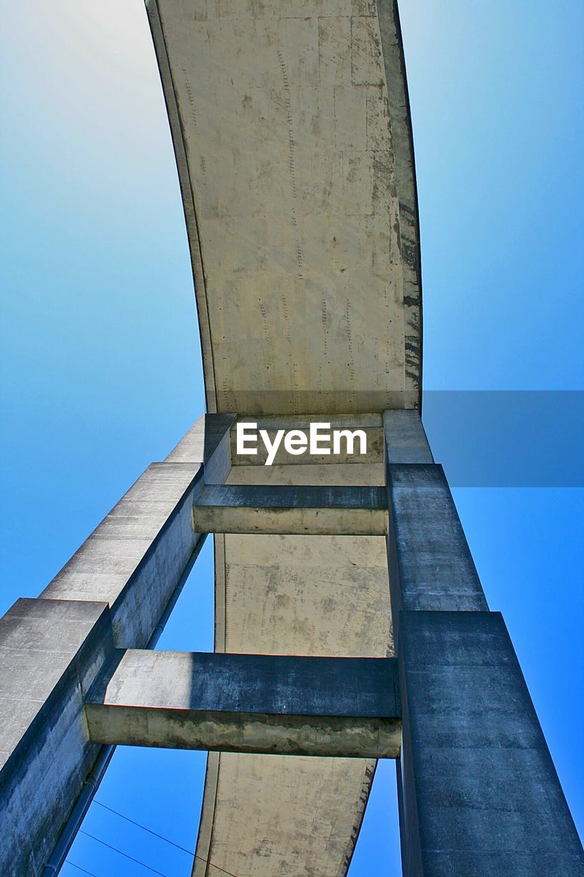 LOW ANGLE VIEW OF BRIDGE AGAINST BUILDING AGAINST CLEAR BLUE SKY