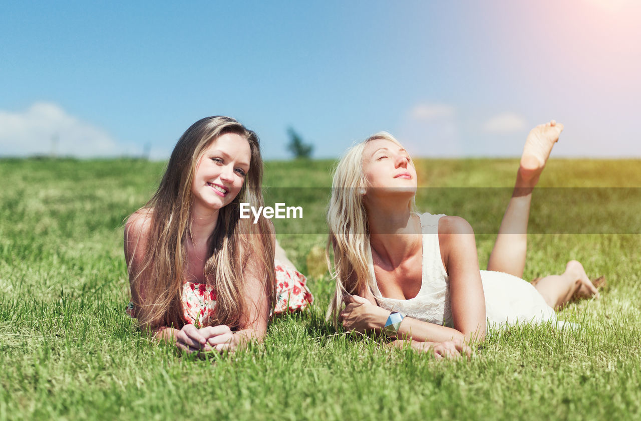 Portrait of smiling woman with friend lying on grass against sky