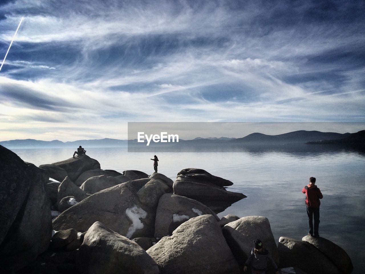 People on rocks by lake against sky