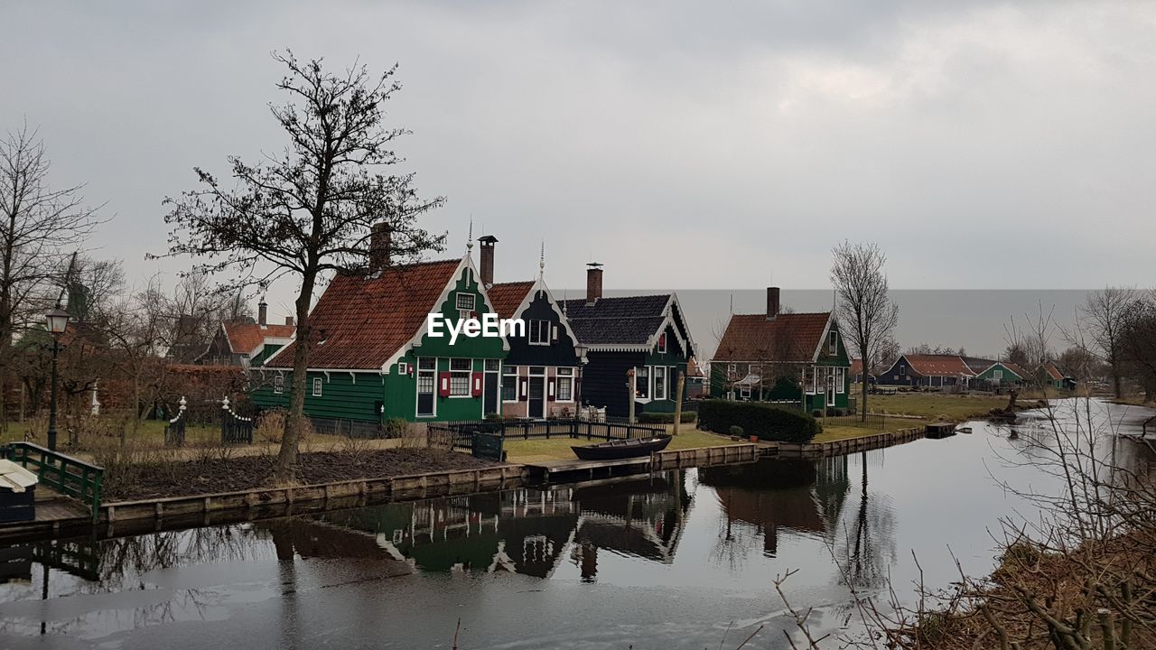 Reflection of houses on canal against cloudy sky 