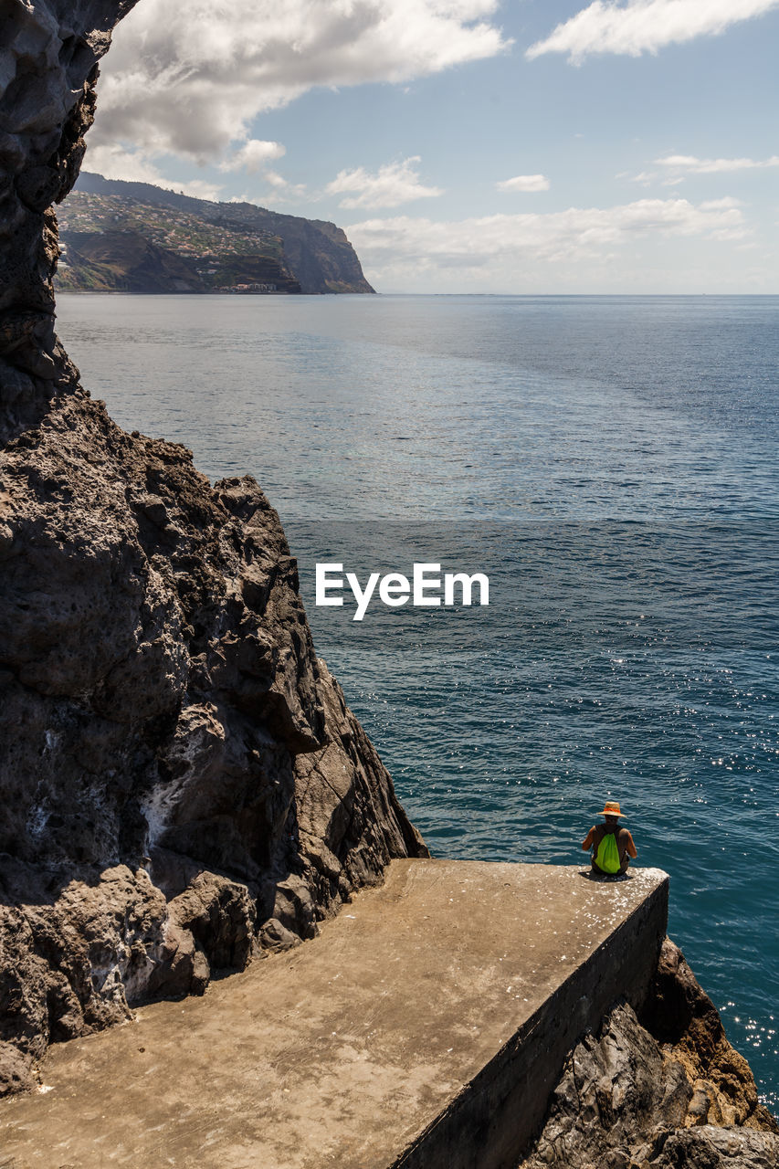 High angle view of man sitting on cliff against sea