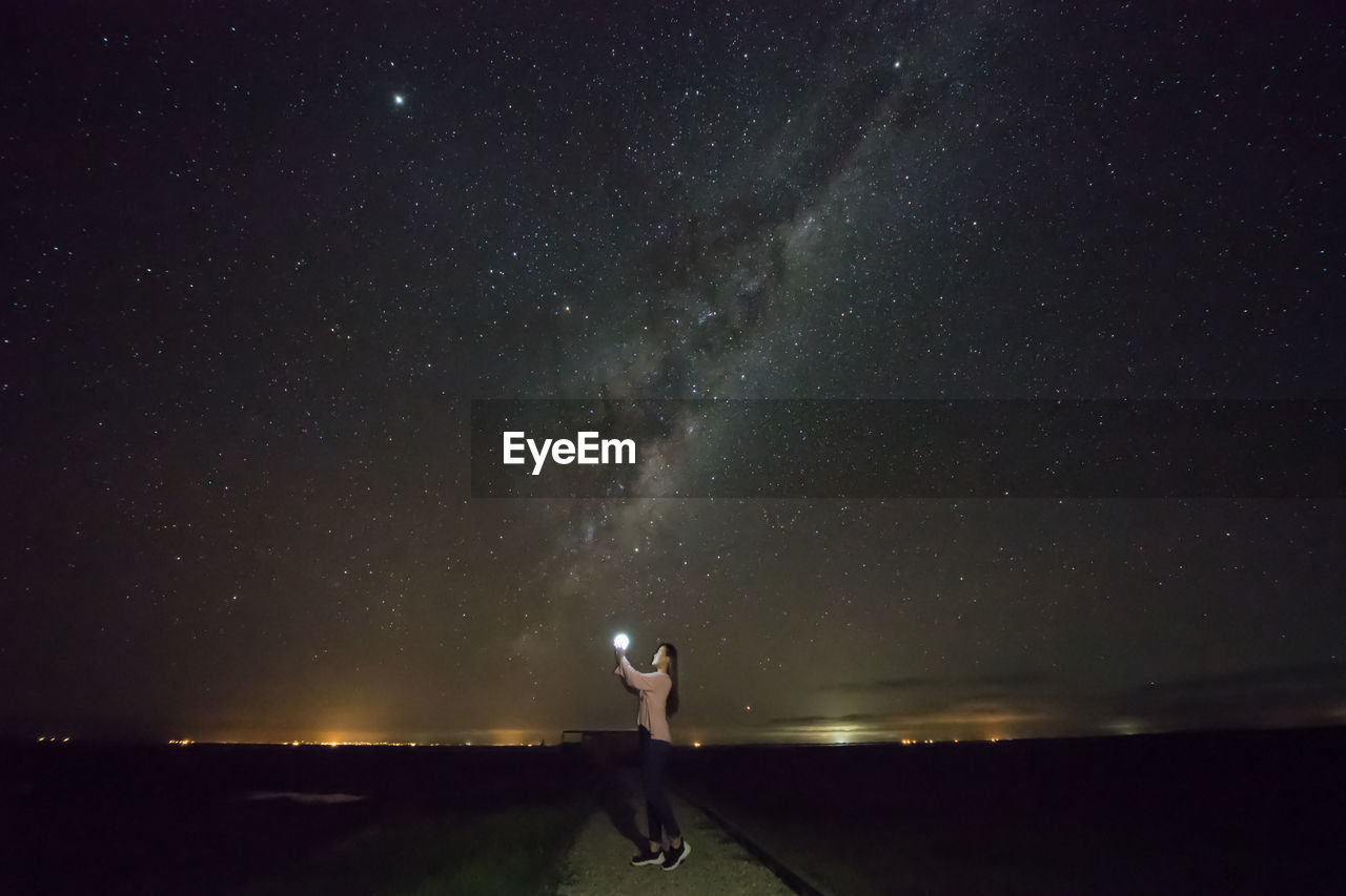 Side view of woman holding light while standing against star field