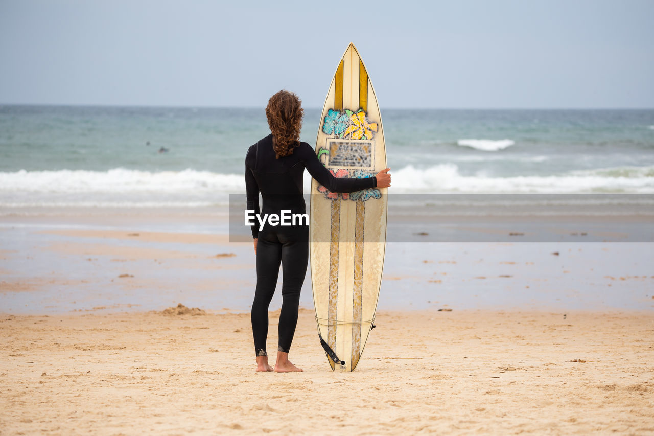 Rear view of man standing with surfboard at beach