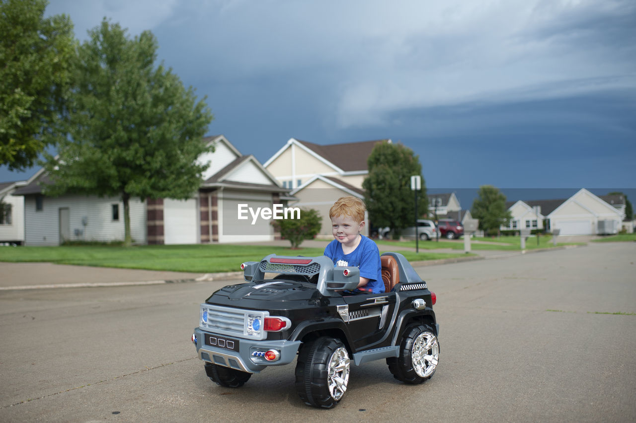 Young boy drives electric toy car down neighborhood street