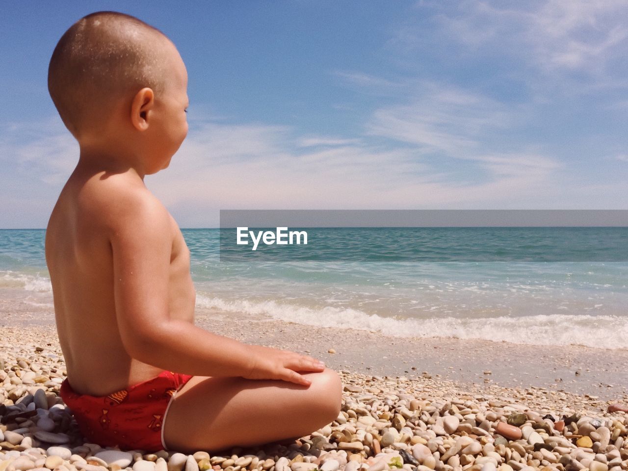 Shirtless child sitting on shore at beach during sunny day