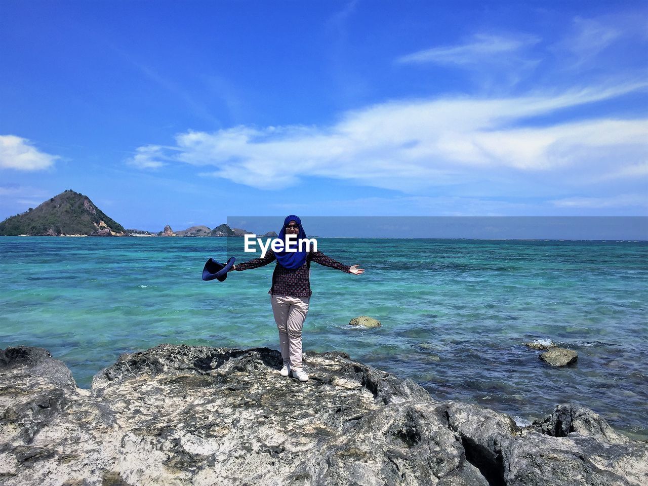 Full length of woman standing on rock at beach against sky