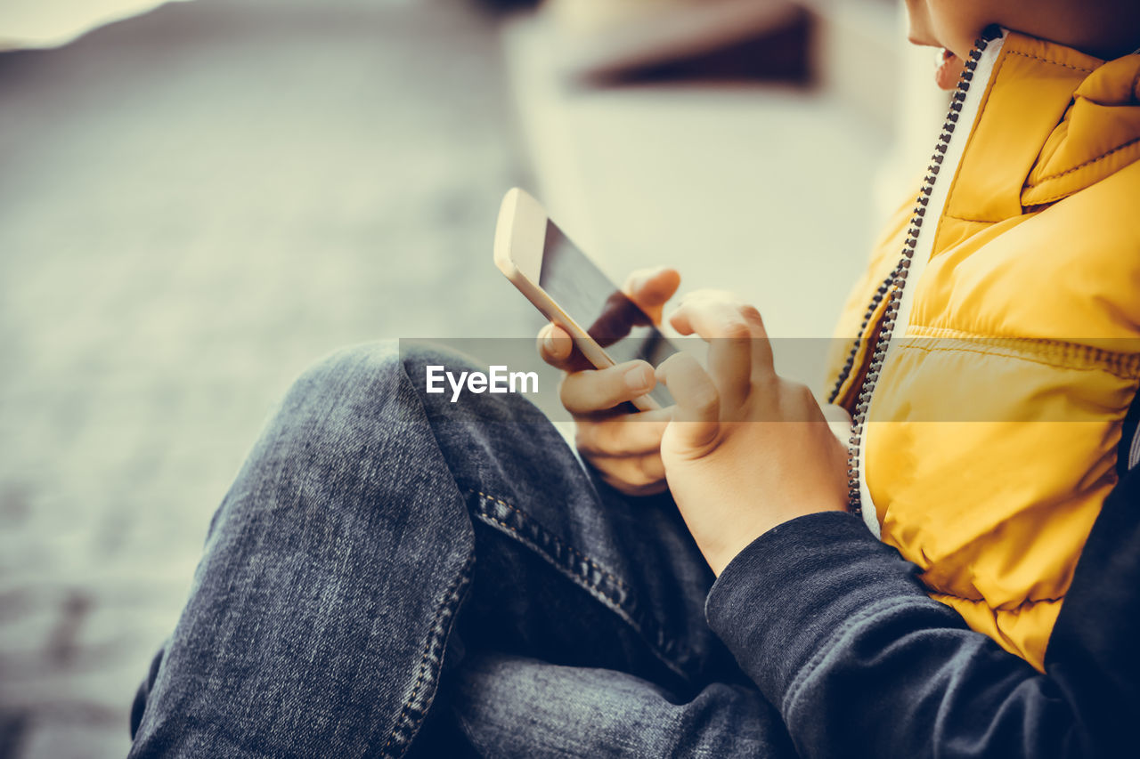 Close-up of kid using smart phone while relaxing outdoors.