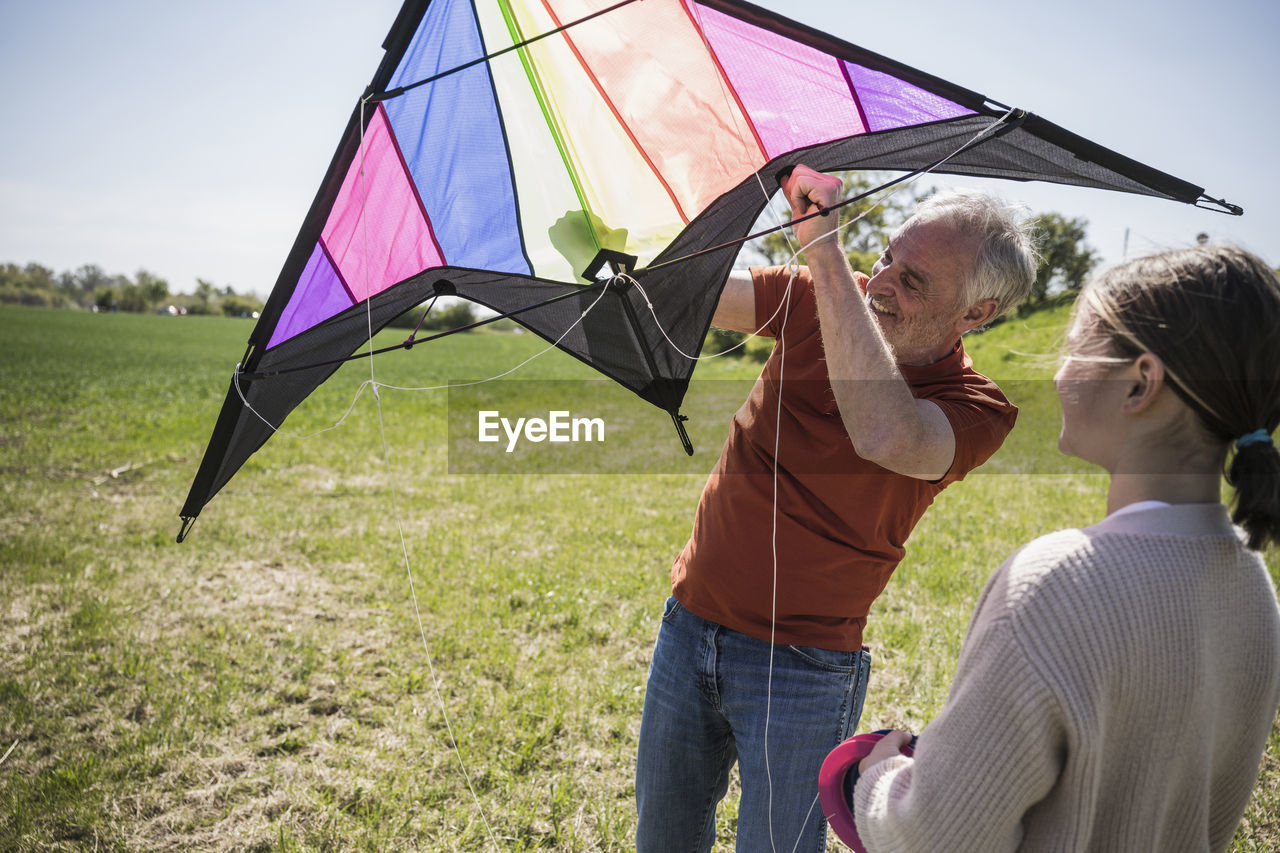 Grandfather assisting granddaughter with kite on field