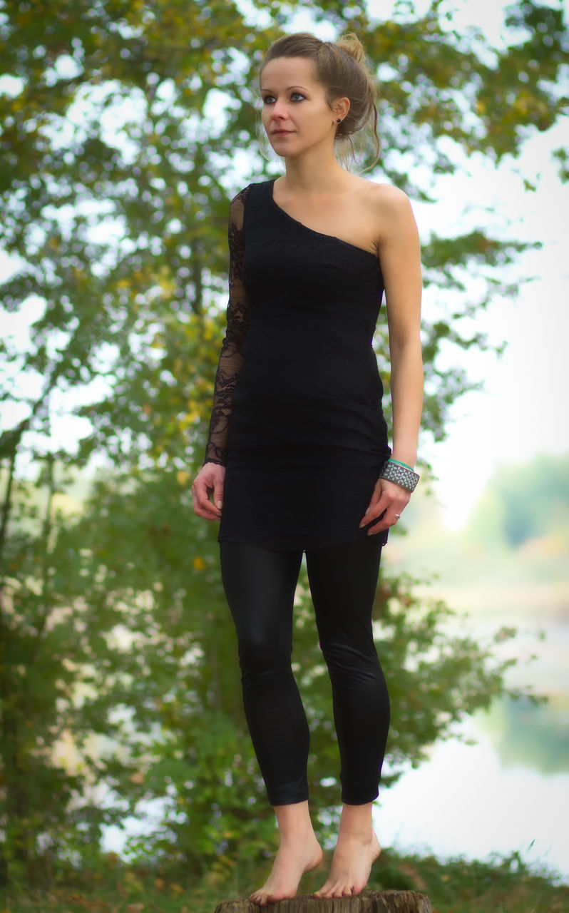 Full length of young woman standing on tree stump