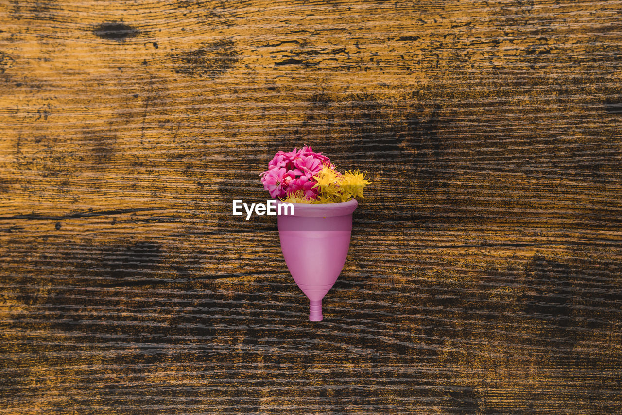 Menstrual cup with flowers on wooden background