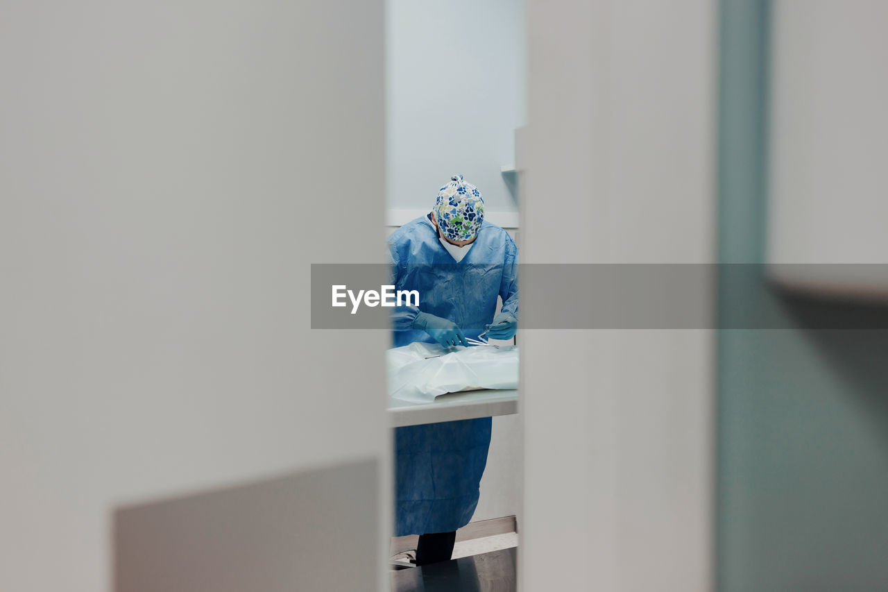 Focused male veterinarian in uniform and respiratory mask using medical instruments during surgery in hospital