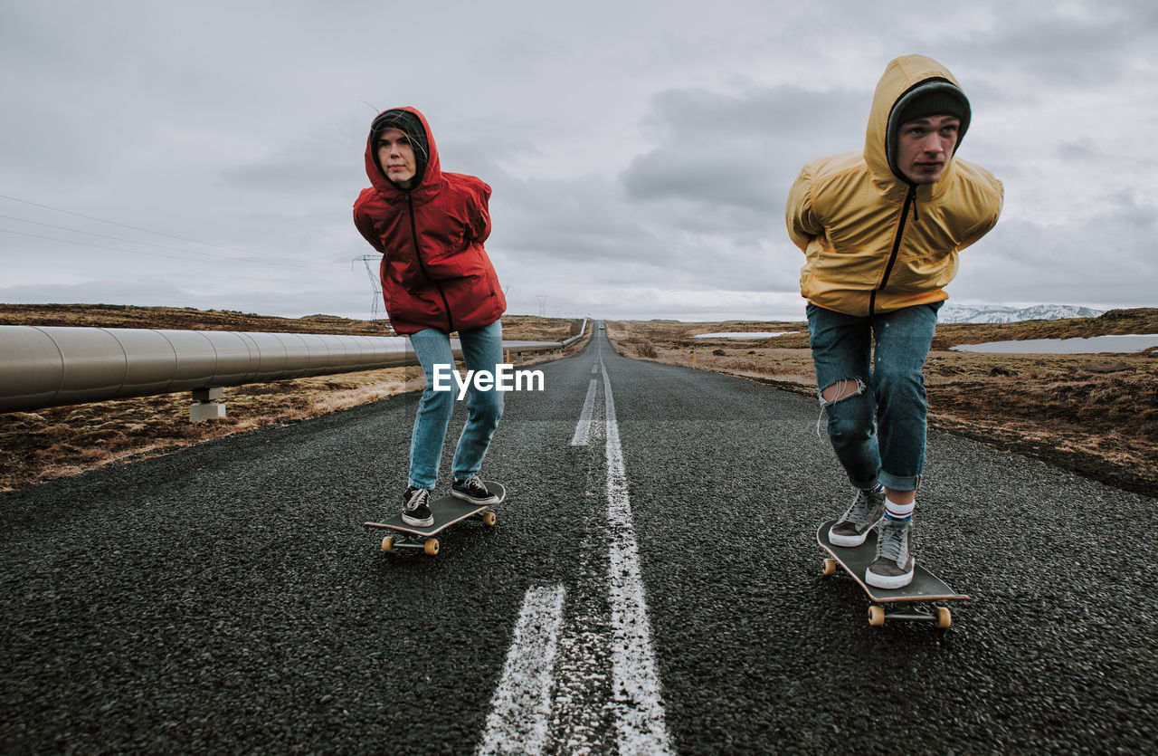 Full length of couple skateboarding on road against sky