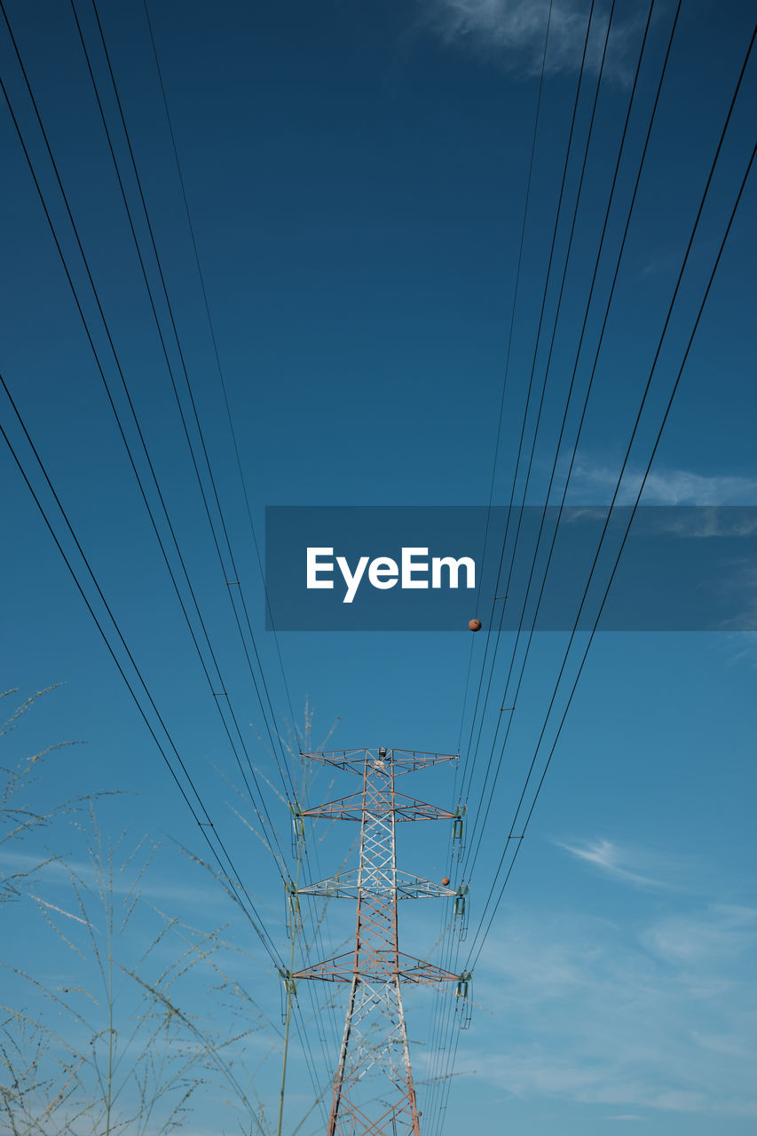 Low angle view of electricity pylon against blue sky