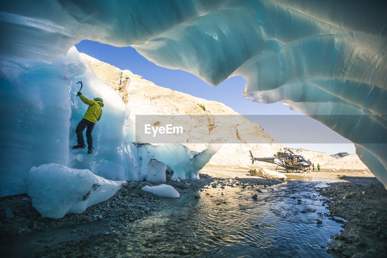 Ice climber climbing on glacial ice next to helicopter.
