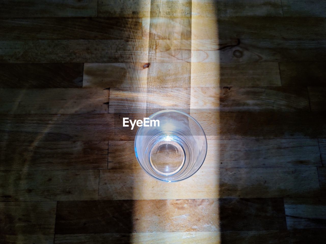 High angle view of glass on wooden table in sunlight beam