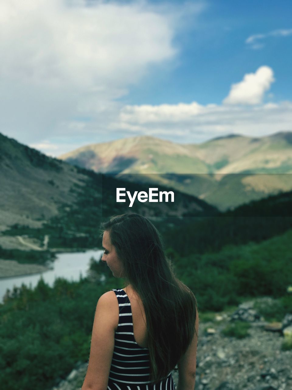 Rear view of young woman standing on mountain against cloudy sky