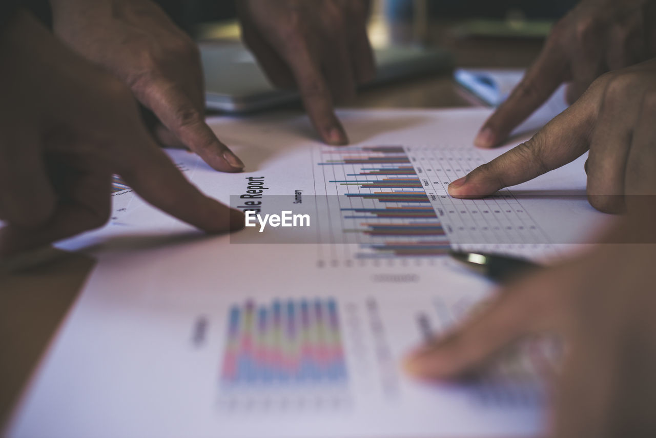 Cropped hands pointing at graph charts at table in office