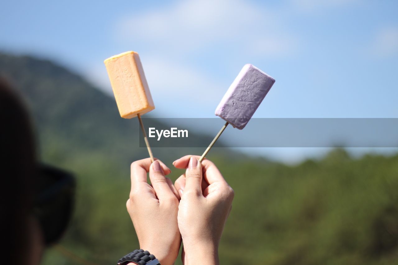 Close-up of hand holding popsicles against sky