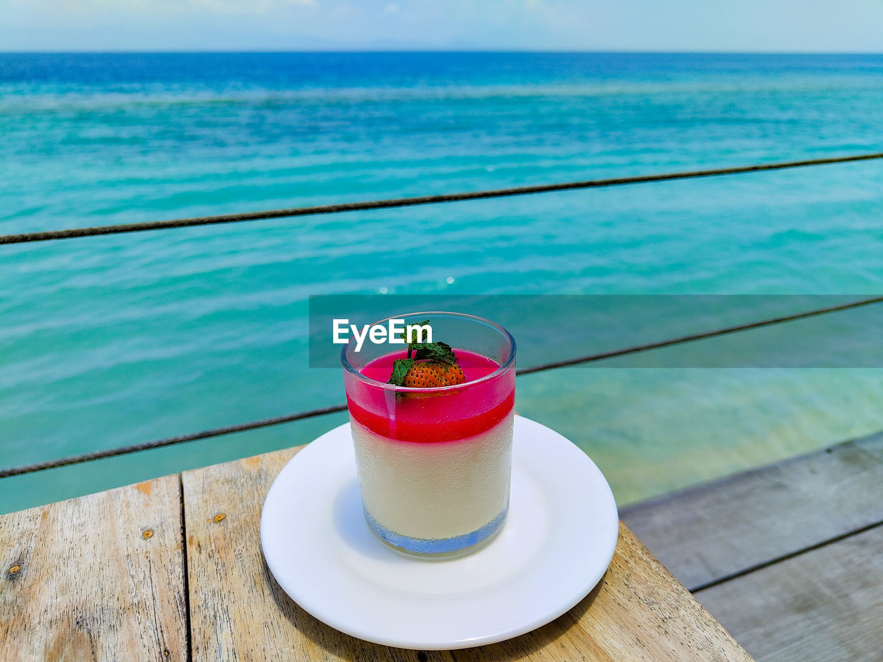 water, food and drink, sea, drink, refreshment, horizon over water, horizon, nature, food, summer, freshness, wood, drinking glass, sky, table, beauty in nature, land, day, glass, no people, household equipment, wellbeing, fruit, blue, swimming pool, vacation, trip, tranquility, outdoors, holiday, healthy eating, railing, scenics - nature, sunlight, beach, tranquil scene, cup, cocktail, tropical climate, travel destinations, straw, relaxation, travel, idyllic, drinking straw, red, focus on foreground