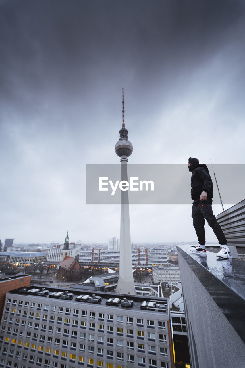 Low angle view of young man standing on building against cloudy sky