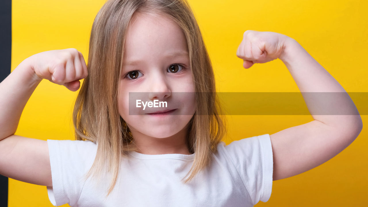 childhood, child, portrait, yellow, one person, looking at camera, women, smiling, female, emotion, happiness, cute, person, teenager, front view, indoors, headshot, innocence, colored background, hairstyle, blond hair, human face, casual clothing, studio shot, fun, toddler, cheerful, long hair, arm, finger, positive emotion, standing, human hair, education, skin, close-up