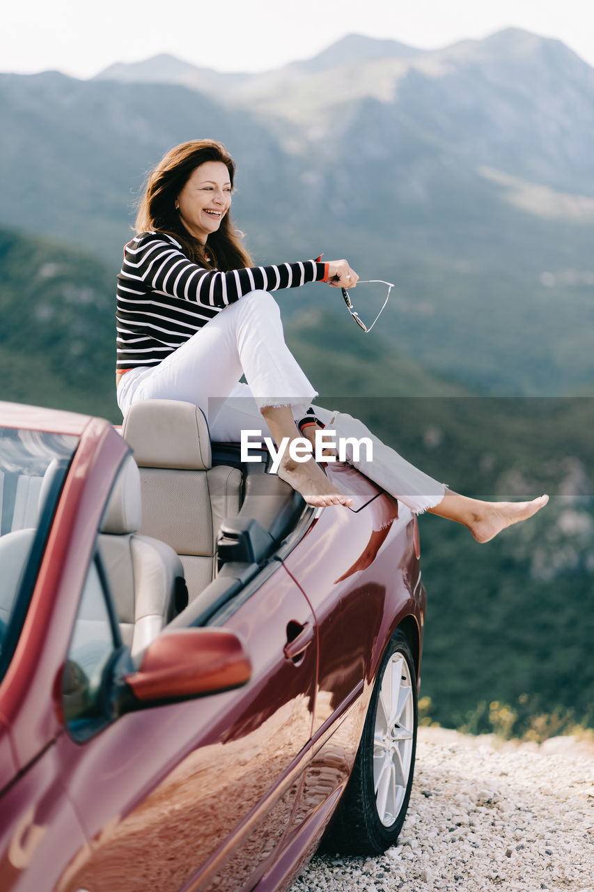 WOMAN SITTING ON MOTORCYCLE AGAINST MOUNTAIN