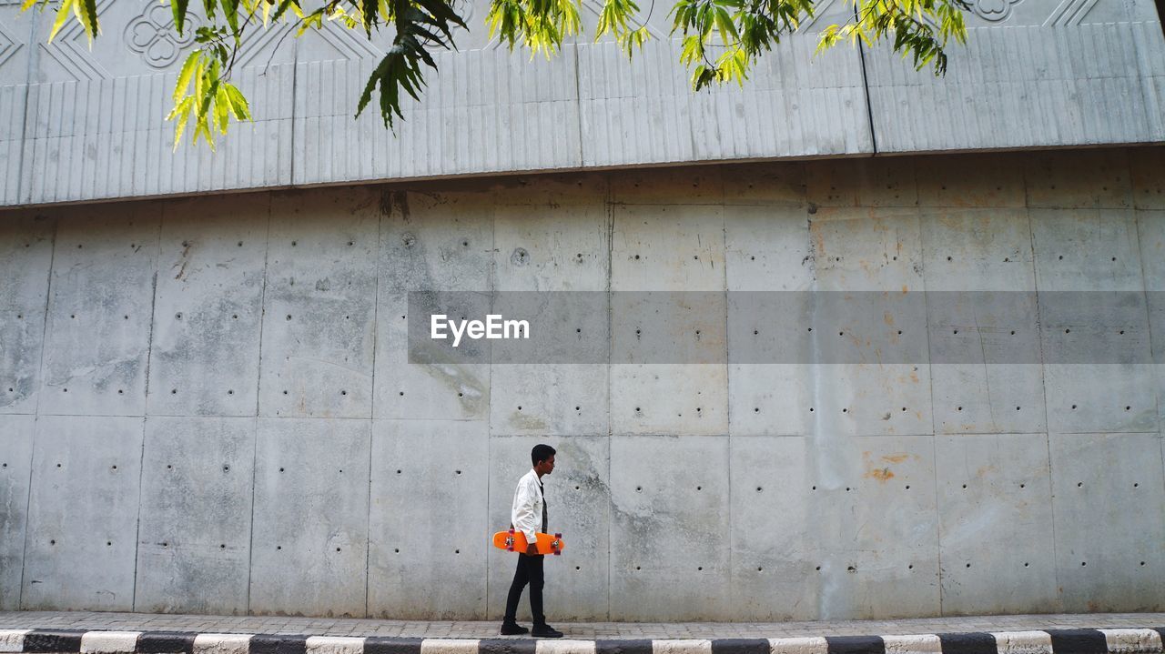 Full length of boy walking on footpath against wall
