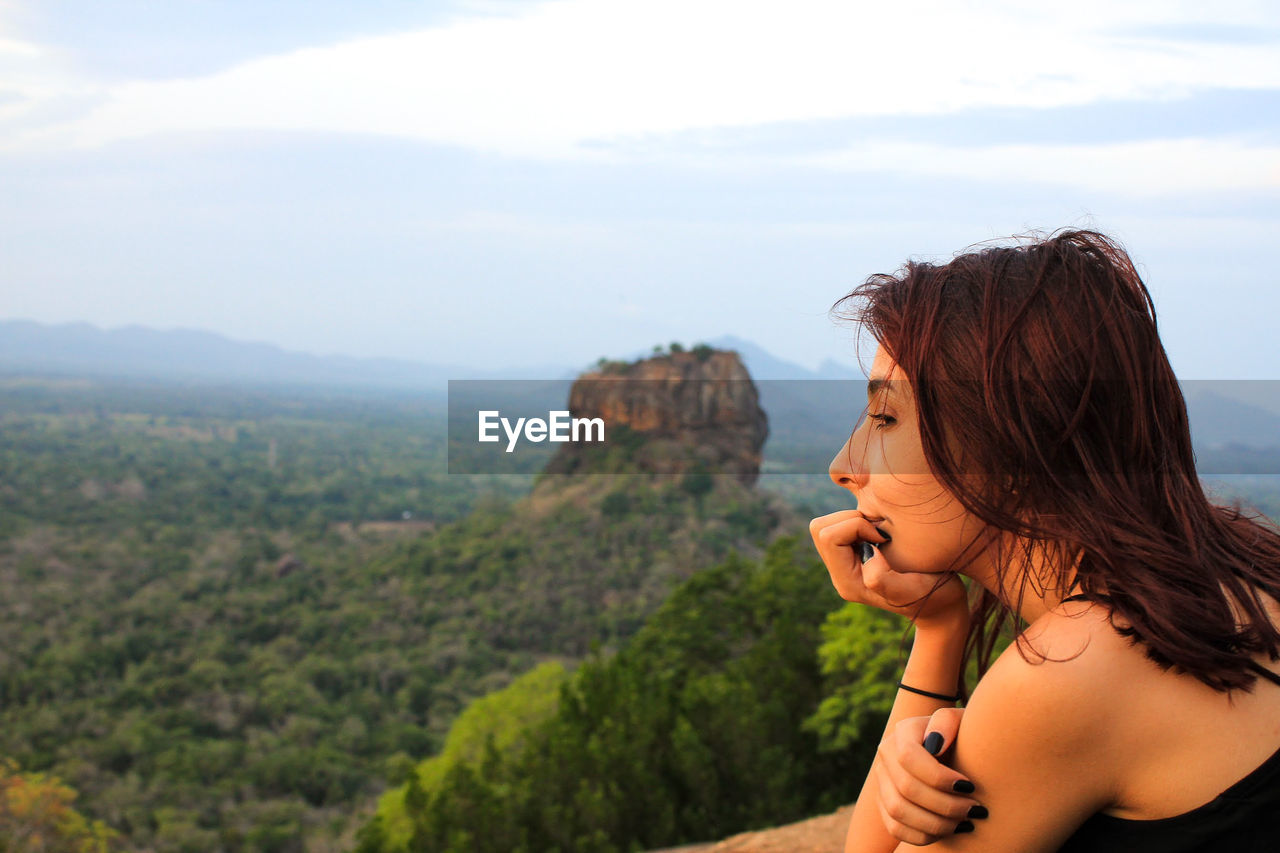 Side view of young woman looking at mountain against sky