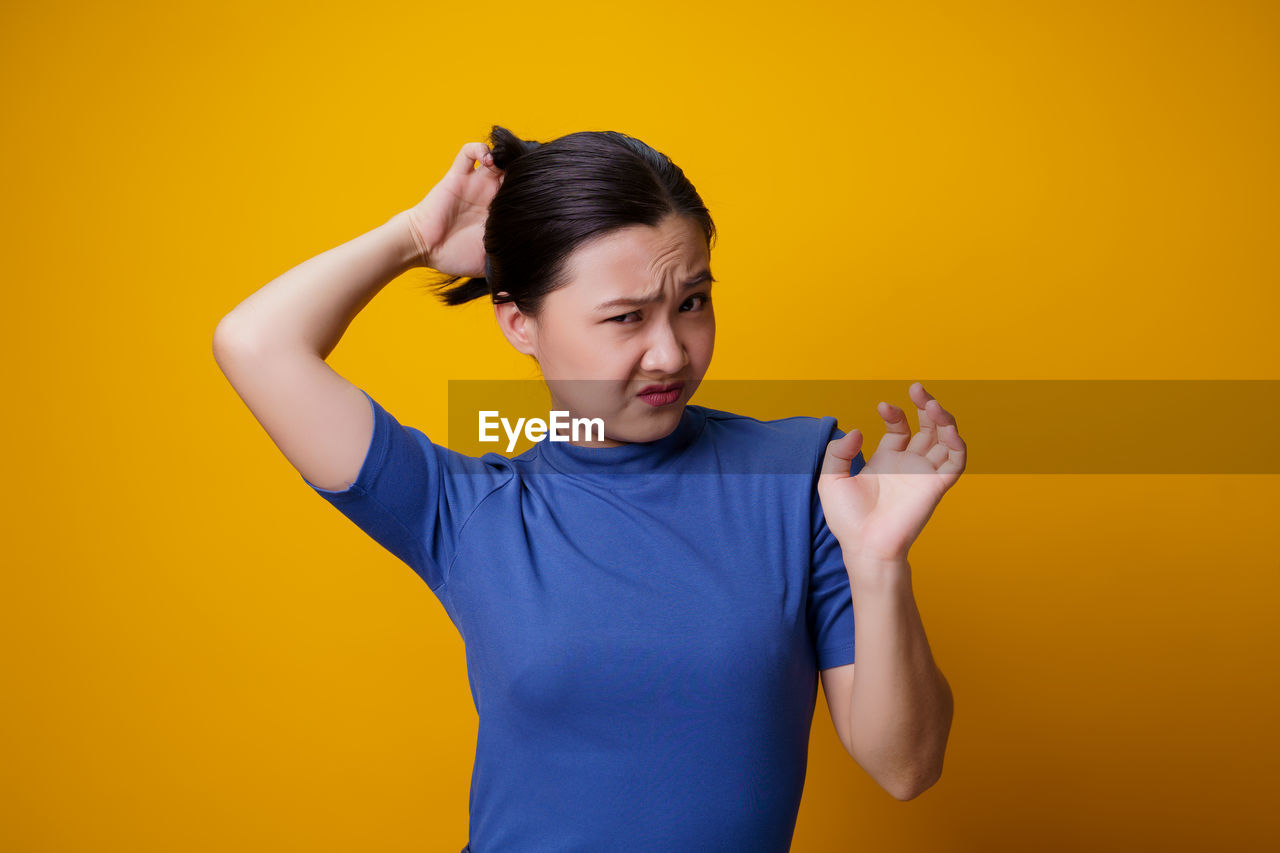 MID ADULT WOMAN STANDING AGAINST YELLOW WALL AGAINST ORANGE BACKGROUND