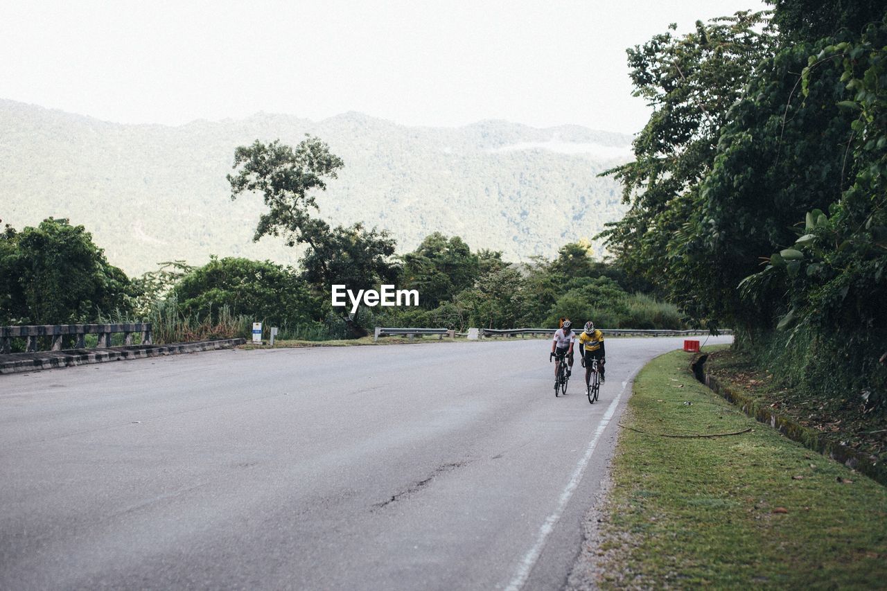 REAR VIEW OF PEOPLE RIDING BICYCLES ON ROAD AGAINST SKY