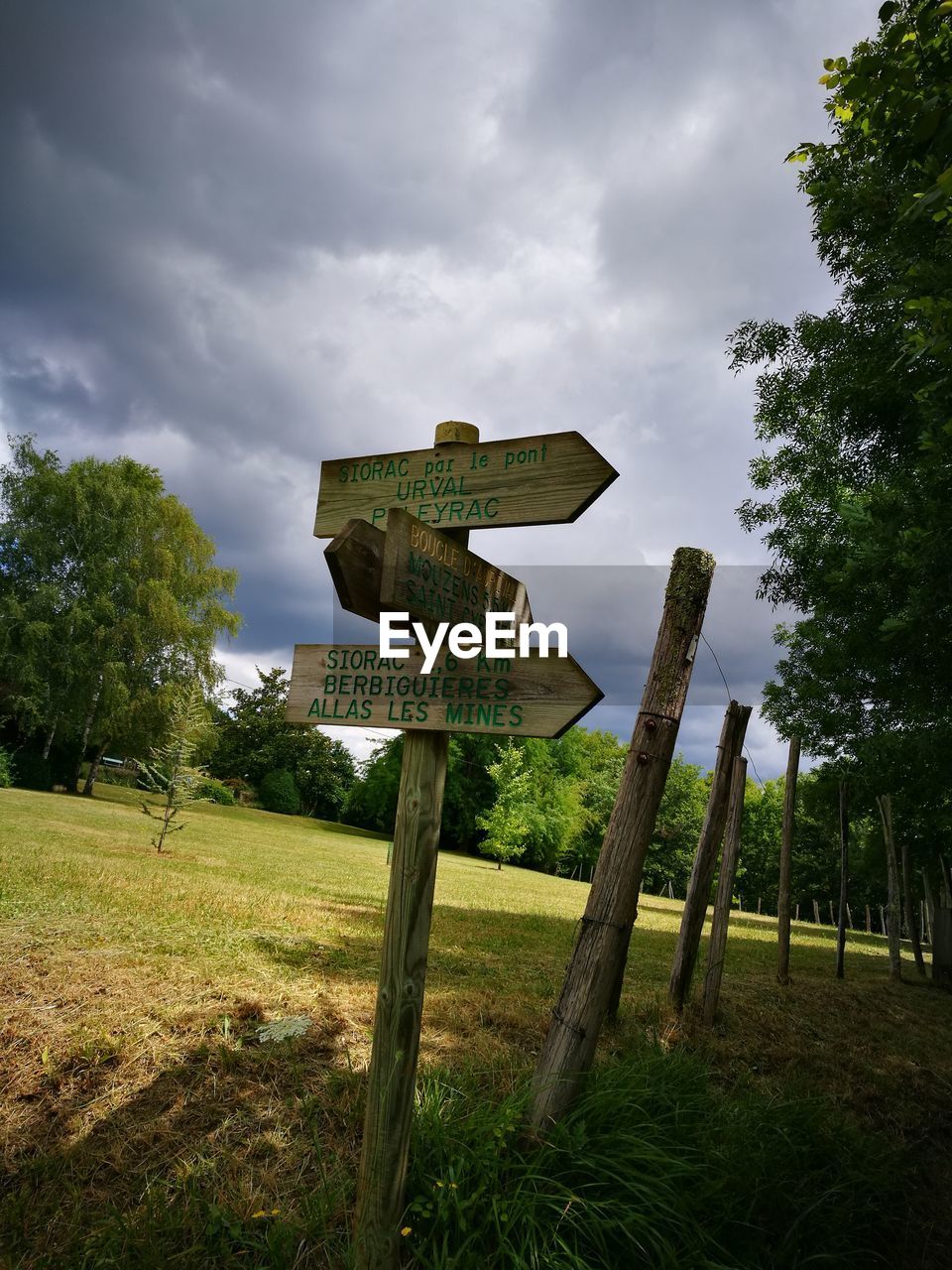 Road sign on wooden post in field against sky