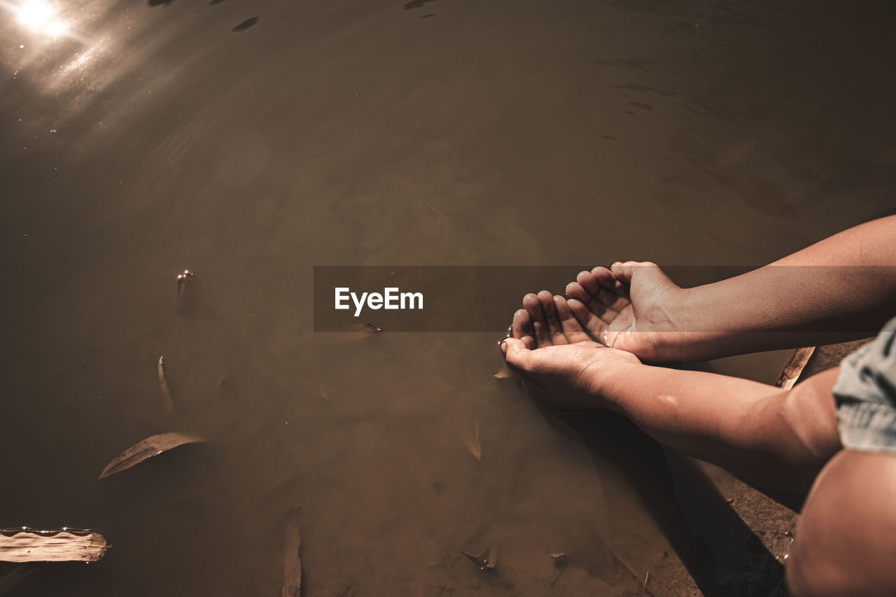 Cropped image of hands holding water over lake