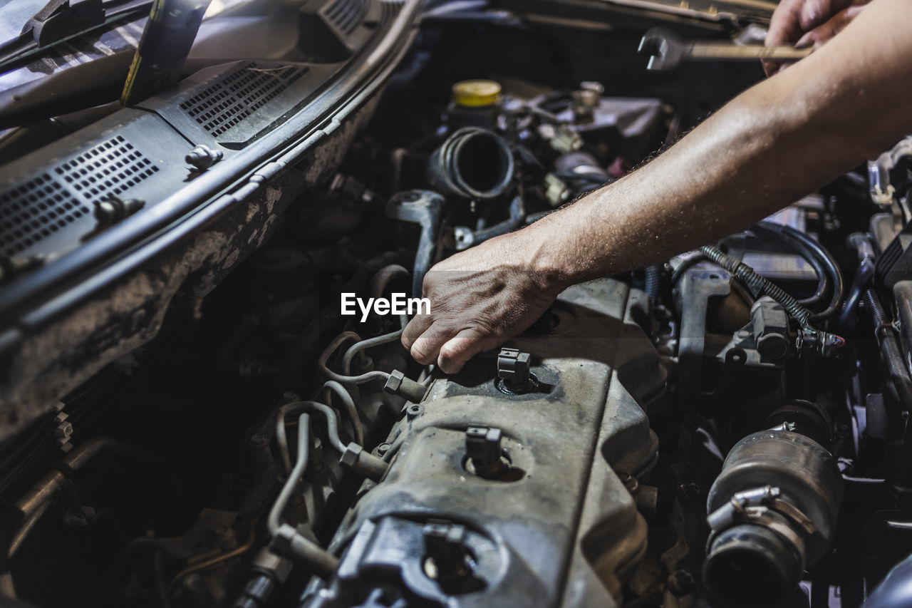 Unrecognizable male technician putting cables into motor while fixing vehicle during work in garage