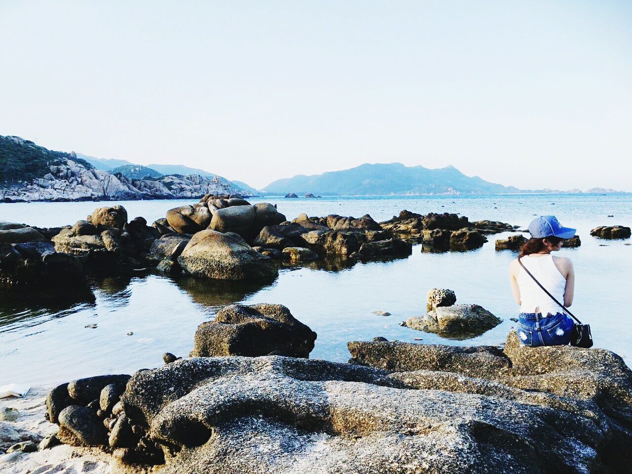 Rear view of woman sitting on rock in lake