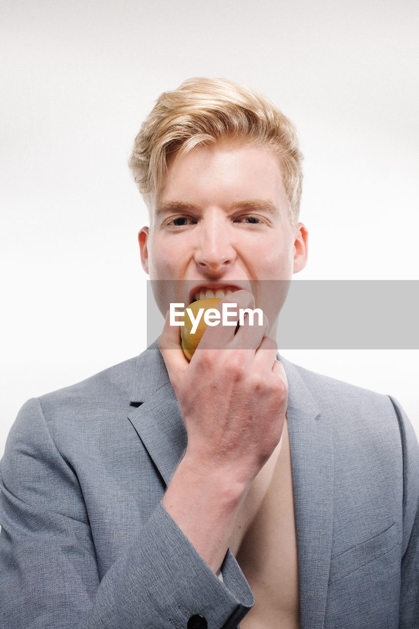 Portrait of handsome young man eating fruit against white background