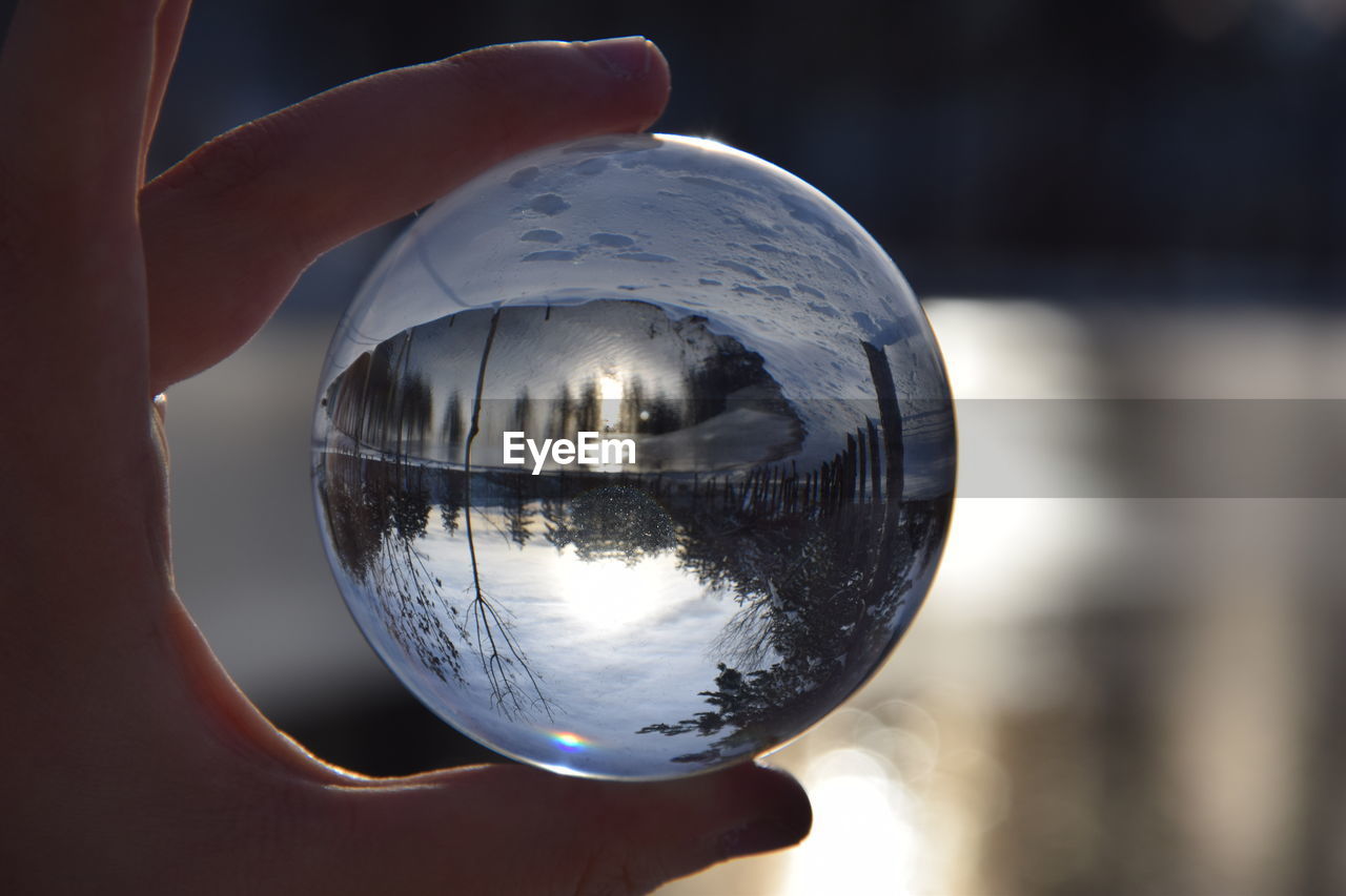 REFLECTION OF PERSON HAND HOLDING CRYSTAL BALL IN GLASS