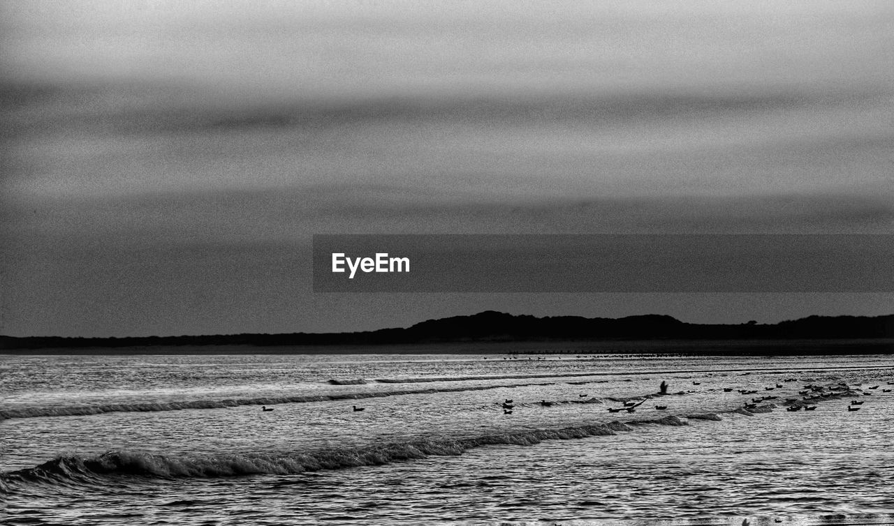 DISTANT VIEW OF CALM BEACH AGAINST CLOUDY SKY