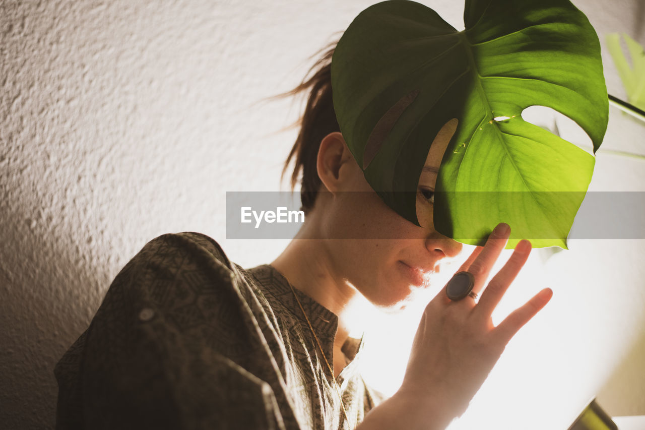 Asian woman peaks through plant leaf in lamp light at home