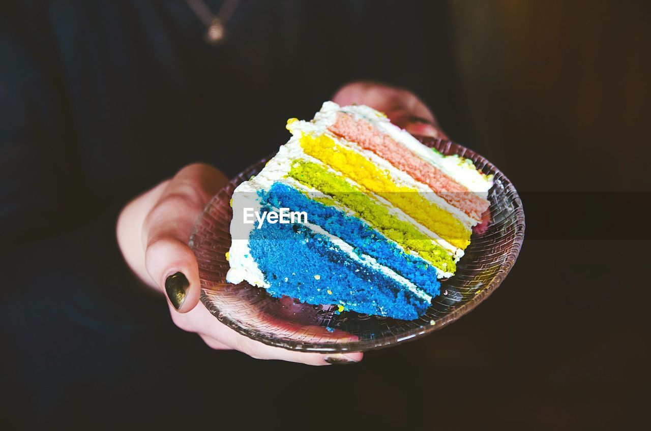 Midsection of woman holding rainbow cake in plate