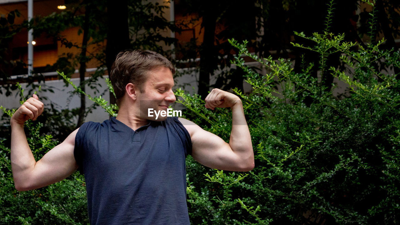 YOUNG MAN STANDING BY PLANTS IN PARK