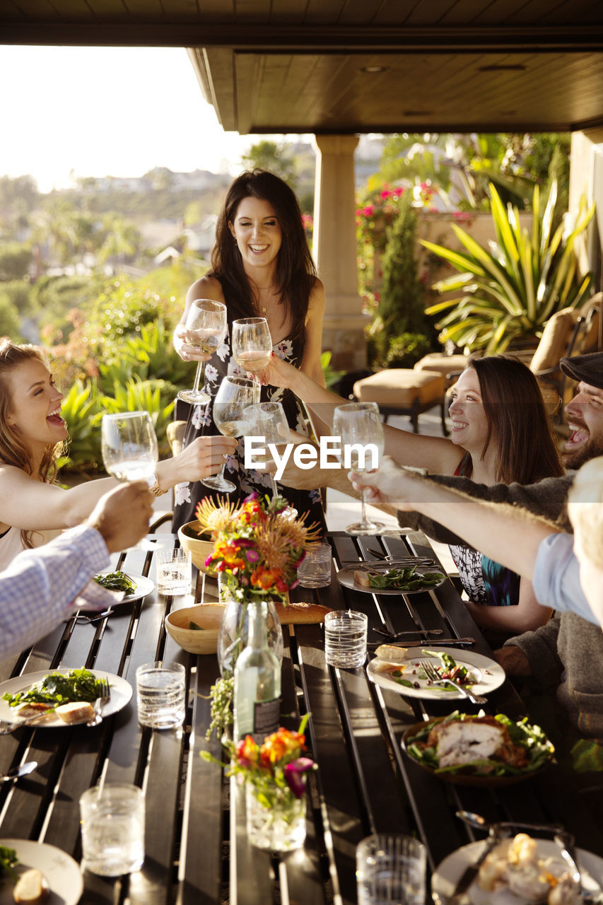 Happy friends toasting wineglasses at dining table on porch