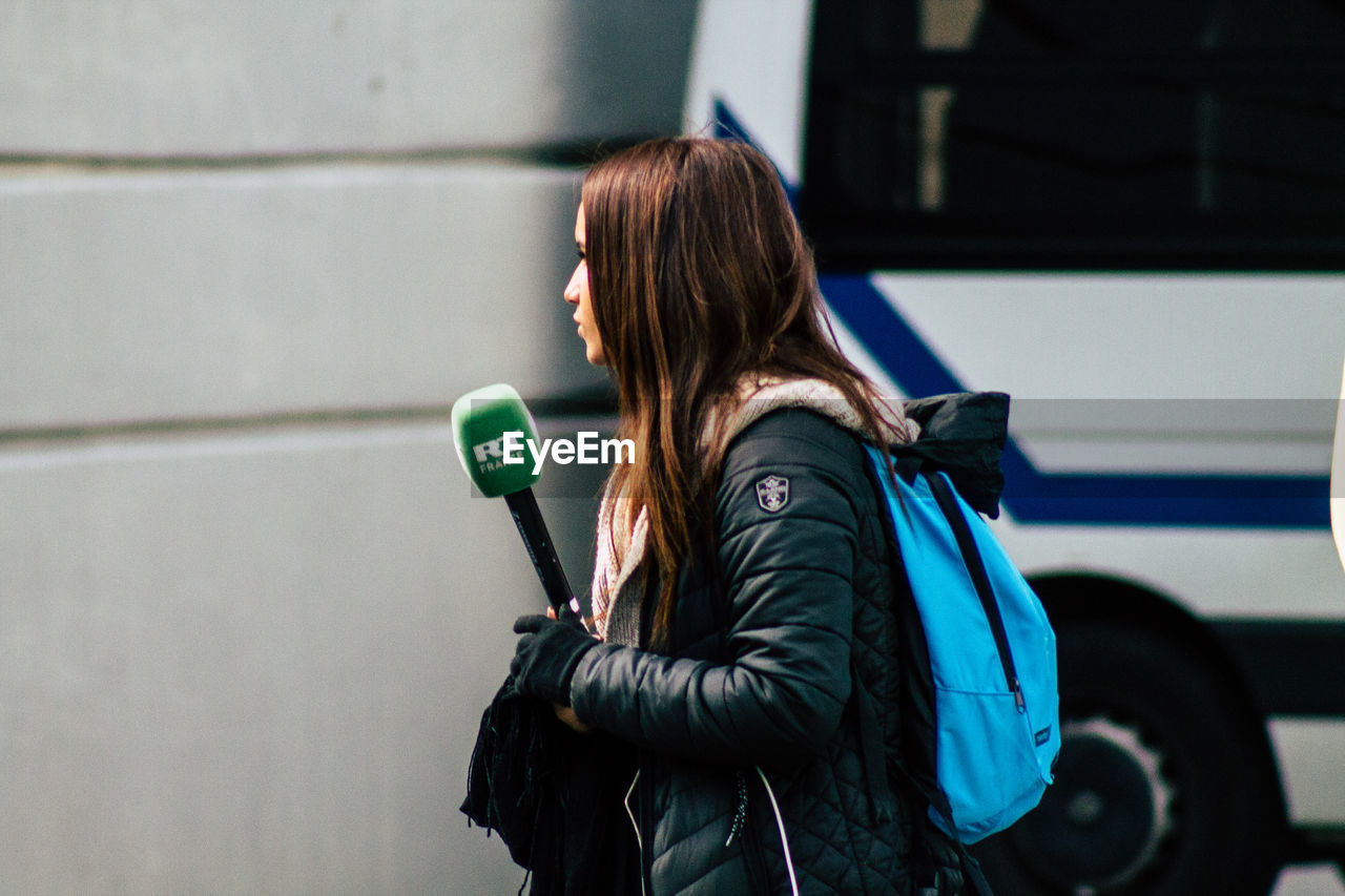 REAR VIEW OF WOMAN STANDING AGAINST WALL