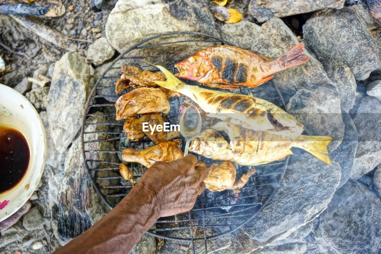 Cropped hand grilling fish on fire pit